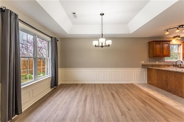 kitchen featuring sink, a raised ceiling, hanging light fixtures, and light stone counters