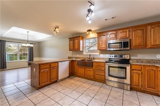 kitchen with kitchen peninsula, a chandelier, stainless steel appliances, a raised ceiling, and sink