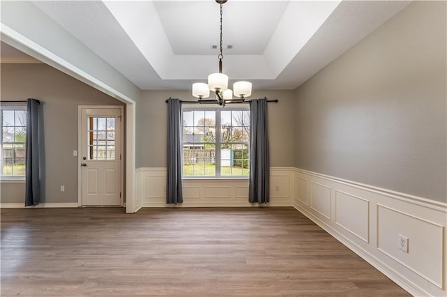 unfurnished dining area with a notable chandelier, a raised ceiling, and hardwood / wood-style flooring