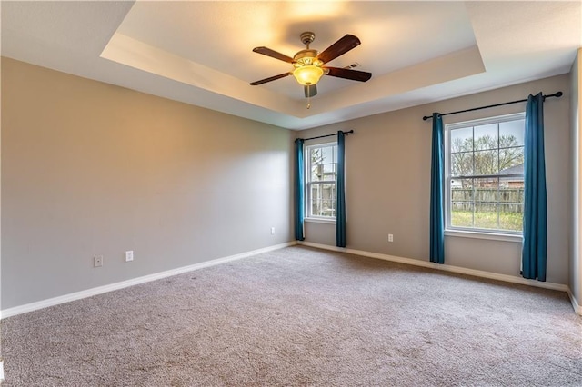 unfurnished room with a raised ceiling, ceiling fan, and plenty of natural light