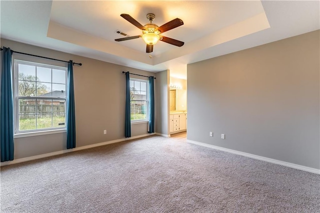 carpeted spare room featuring a raised ceiling, ceiling fan, and plenty of natural light