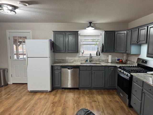 kitchen featuring light stone countertops, appliances with stainless steel finishes, gray cabinets, and sink