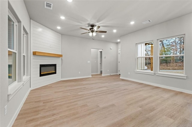 unfurnished living room with a large fireplace, light hardwood / wood-style floors, and ceiling fan