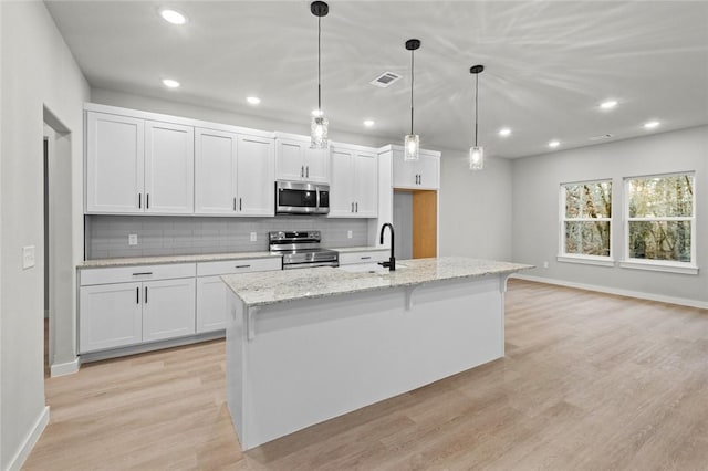 kitchen with appliances with stainless steel finishes, a center island with sink, white cabinetry, and decorative light fixtures