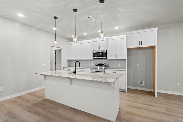 kitchen with appliances with stainless steel finishes, light stone counters, a kitchen island with sink, white cabinets, and hanging light fixtures