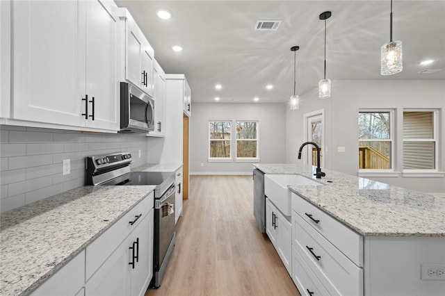 kitchen featuring light stone countertops, stainless steel appliances, white cabinetry, hanging light fixtures, and an island with sink