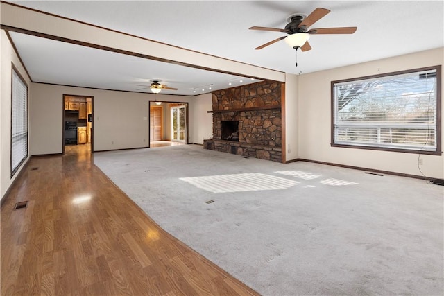 unfurnished living room featuring carpet floors, a stone fireplace, and ceiling fan