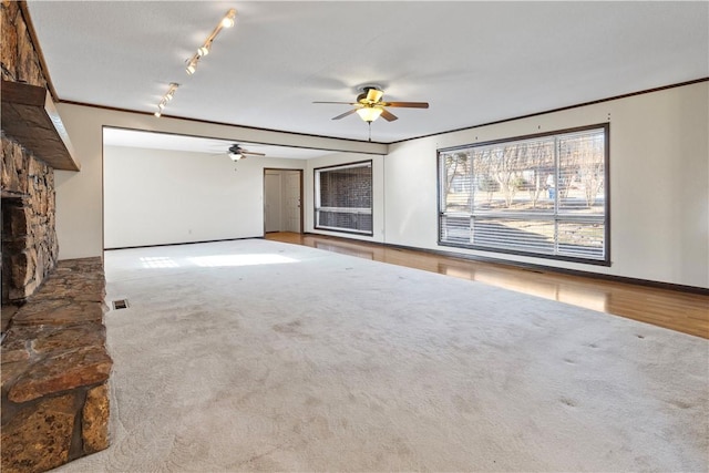 unfurnished living room featuring ceiling fan, a fireplace, light colored carpet, and ornamental molding