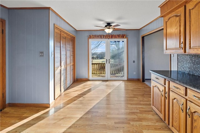 kitchen with french doors, light wood-type flooring, ceiling fan, crown molding, and dark stone countertops