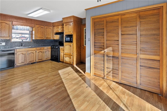 kitchen with decorative backsplash, sink, black appliances, and light hardwood / wood-style floors