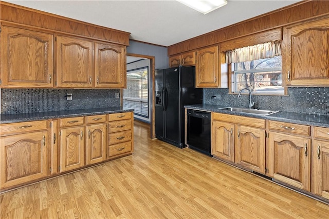 kitchen featuring dark stone counters, black appliances, crown molding, sink, and light hardwood / wood-style floors