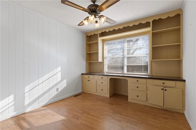 unfurnished office with built in shelves, ceiling fan, light hardwood / wood-style flooring, a textured ceiling, and built in desk