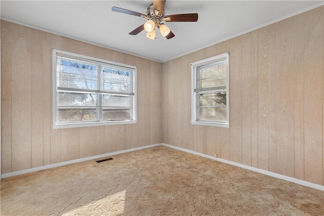 carpeted spare room with ceiling fan, wood walls, and ornamental molding