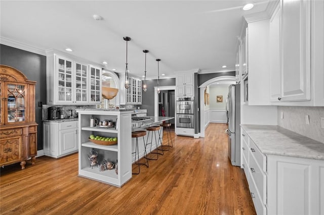 kitchen featuring appliances with stainless steel finishes, light stone counters, a kitchen island, pendant lighting, and white cabinetry