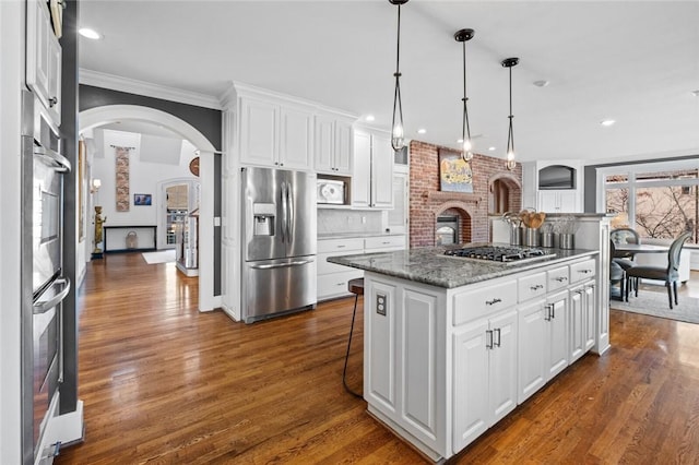 kitchen with appliances with stainless steel finishes, stone counters, a center island, white cabinetry, and hanging light fixtures