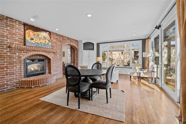 dining room with a fireplace, light wood-type flooring, ornamental molding, and brick wall