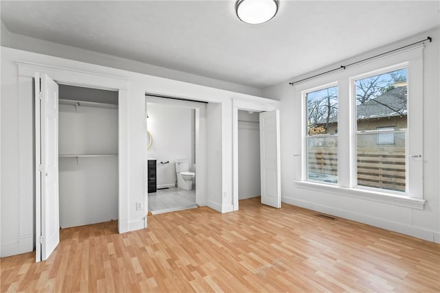 unfurnished bedroom featuring light wood-type flooring, two closets, and ensuite bathroom