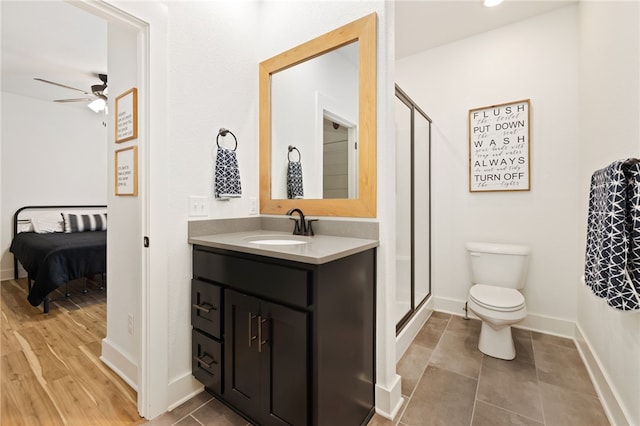 bathroom featuring ceiling fan, vanity, a shower with door, and toilet