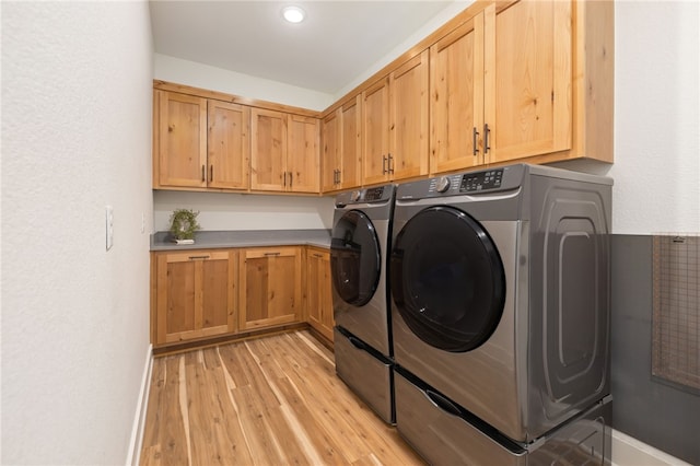 clothes washing area featuring washing machine and dryer, cabinets, and light hardwood / wood-style floors