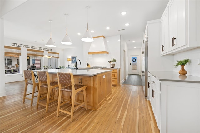 kitchen with decorative light fixtures, a spacious island, light hardwood / wood-style flooring, custom range hood, and white cabinets