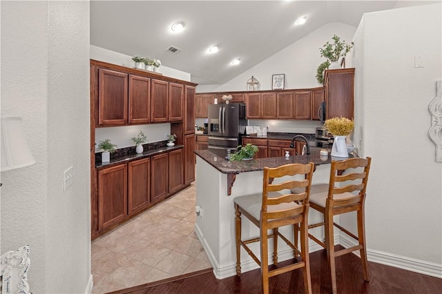 kitchen featuring a kitchen breakfast bar, sink, vaulted ceiling, dark stone countertops, and stainless steel fridge with ice dispenser