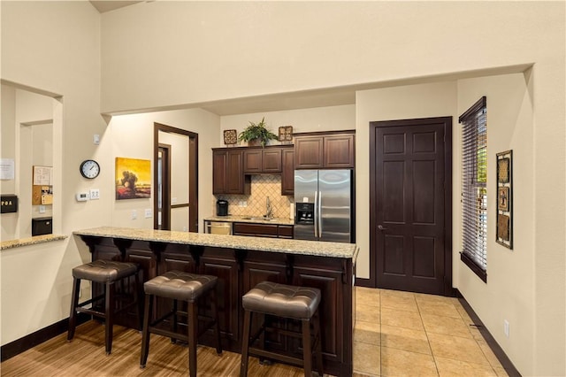 kitchen featuring dark brown cabinetry, sink, a kitchen breakfast bar, stainless steel fridge with ice dispenser, and decorative backsplash