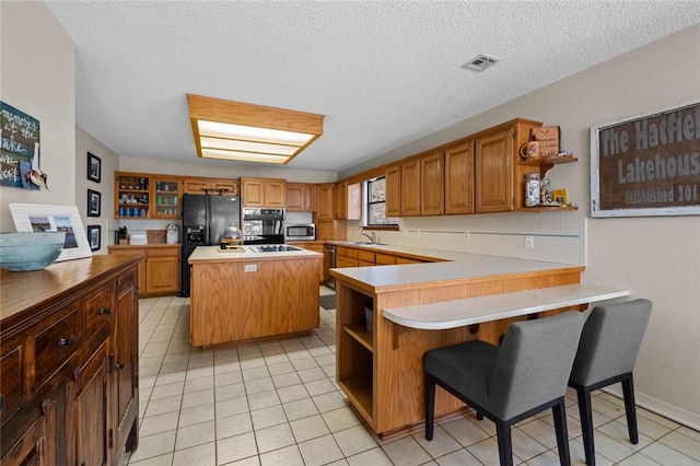 kitchen featuring kitchen peninsula, light tile patterned floors, black appliances, and a textured ceiling