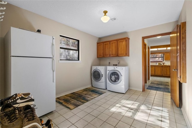 clothes washing area featuring washer and dryer, light tile patterned flooring, cabinets, and a textured ceiling