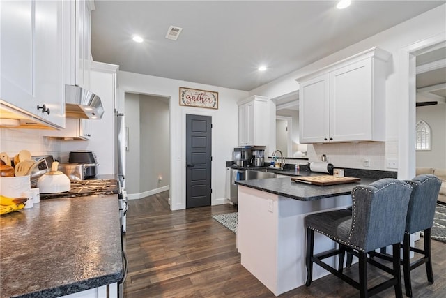 kitchen featuring kitchen peninsula, a breakfast bar, ventilation hood, dark wood-type flooring, and white cabinetry