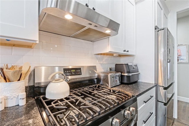 kitchen with decorative backsplash, appliances with stainless steel finishes, dark stone counters, white cabinetry, and range hood