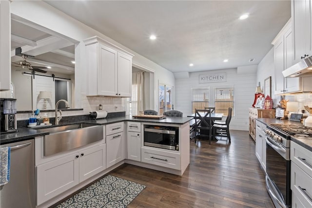 kitchen with white cabinetry, sink, a barn door, kitchen peninsula, and appliances with stainless steel finishes