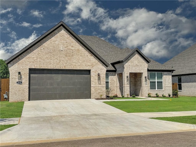 french country home with brick siding, a shingled roof, a front yard, driveway, and an attached garage