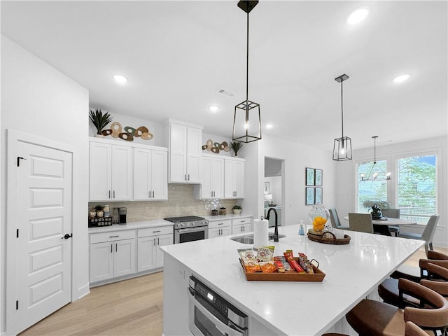 kitchen with visible vents, a breakfast bar, high end range, white cabinetry, and a sink