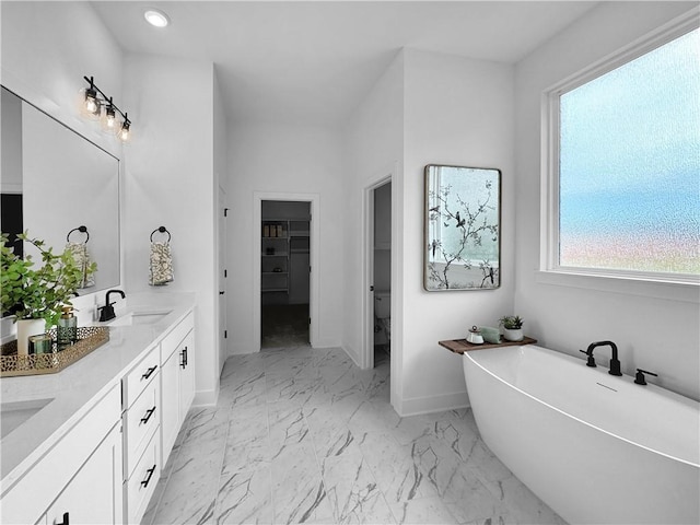 full bathroom with baseboards, double vanity, a freestanding bath, a sink, and marble finish floor