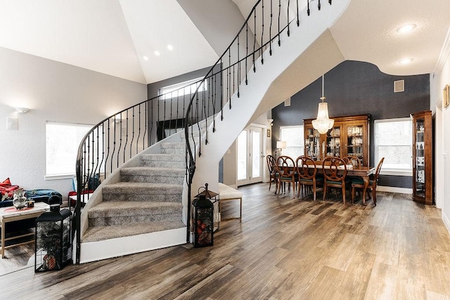 stairway featuring a notable chandelier, wood-type flooring, and high vaulted ceiling