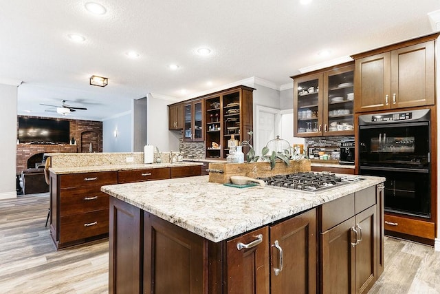 kitchen with backsplash, ceiling fan, double oven, a kitchen island, and stainless steel gas cooktop