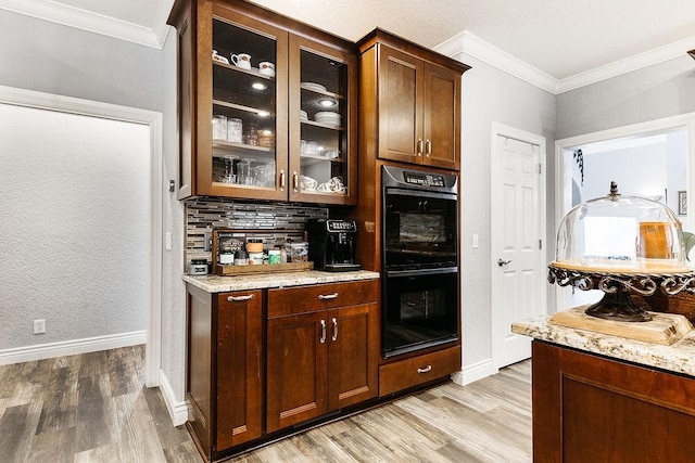 bar with crown molding, light stone counters, black double oven, and light hardwood / wood-style flooring