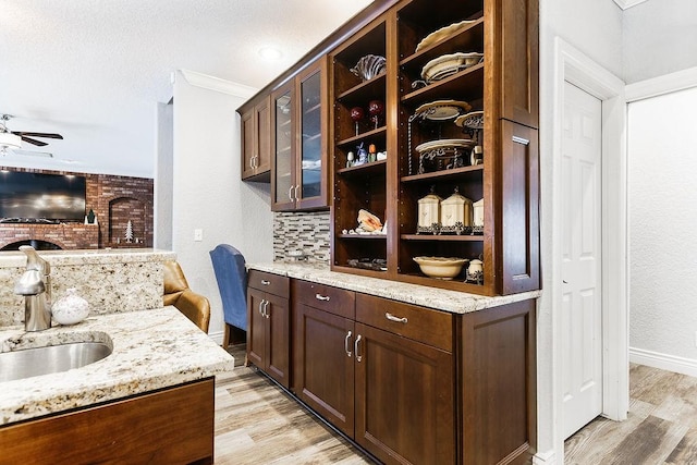 bar with light wood-type flooring, tasteful backsplash, light stone counters, and sink