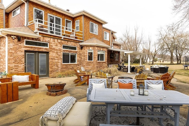 rear view of property featuring a patio area, a balcony, and an outdoor living space with a fire pit