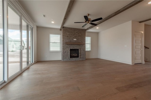 unfurnished living room with beamed ceiling, light hardwood / wood-style flooring, a wealth of natural light, and a brick fireplace