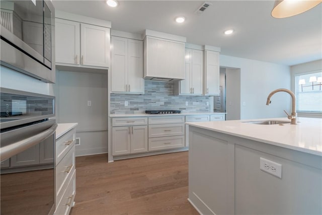 kitchen with decorative backsplash, light wood-type flooring, black gas stovetop, sink, and white cabinets