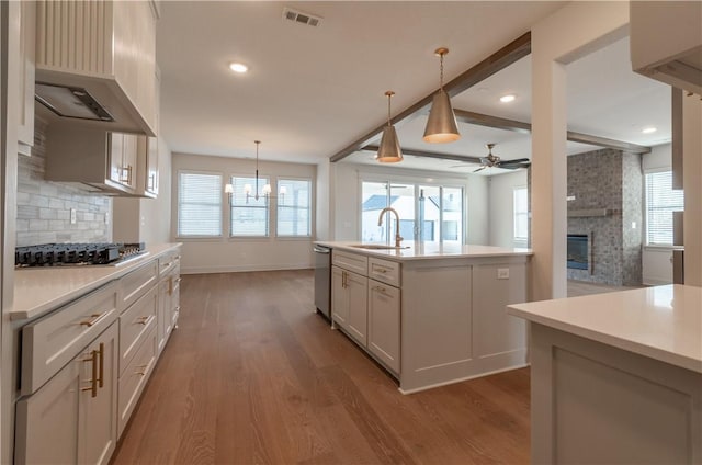 kitchen with sink, wall chimney exhaust hood, stainless steel appliances, pendant lighting, and a center island with sink