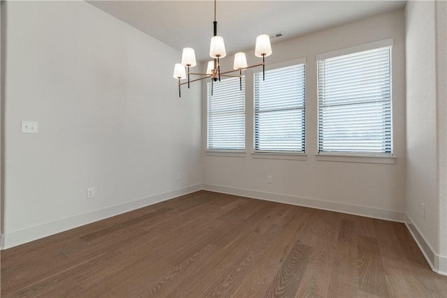 spare room featuring an inviting chandelier and dark wood-type flooring