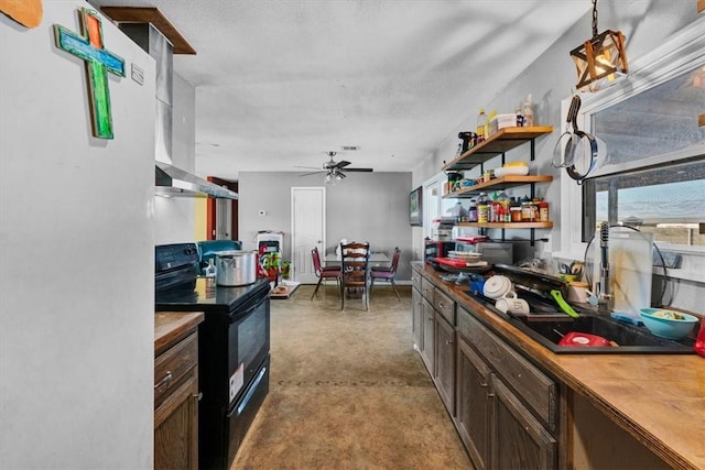 kitchen with wall chimney exhaust hood, black range with electric cooktop, ceiling fan, pendant lighting, and white fridge