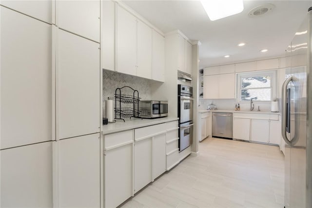 kitchen featuring white cabinetry, sink, stainless steel appliances, backsplash, and light tile patterned flooring