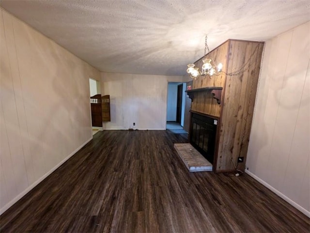 unfurnished living room featuring baseboards, dark wood finished floors, a notable chandelier, a glass covered fireplace, and a textured ceiling