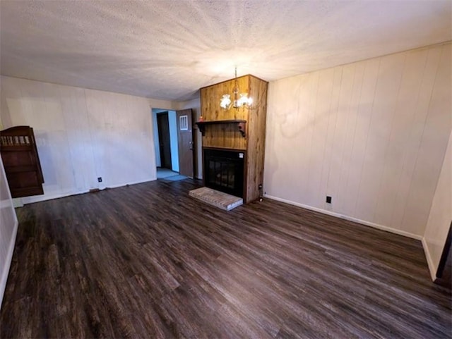 unfurnished living room featuring a fireplace with raised hearth, a textured ceiling, dark wood-type flooring, and an inviting chandelier