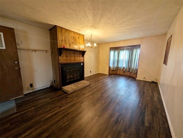 unfurnished living room with a textured ceiling, a brick fireplace, dark wood-style flooring, and an inviting chandelier