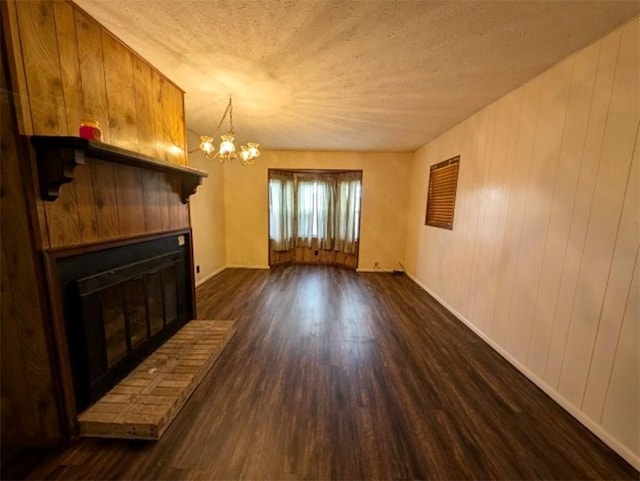 unfurnished living room featuring dark wood-style floors, a notable chandelier, a fireplace, and a textured ceiling