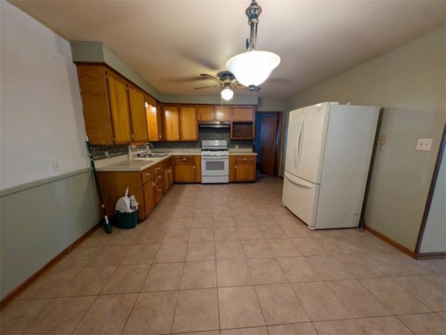 kitchen with brown cabinets, under cabinet range hood, white appliances, light countertops, and decorative backsplash